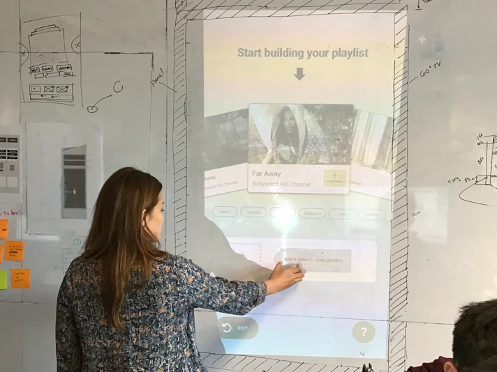 A designer testing the projected playlist flow at body height, sketched panel outlines drawn around it on the wall.
